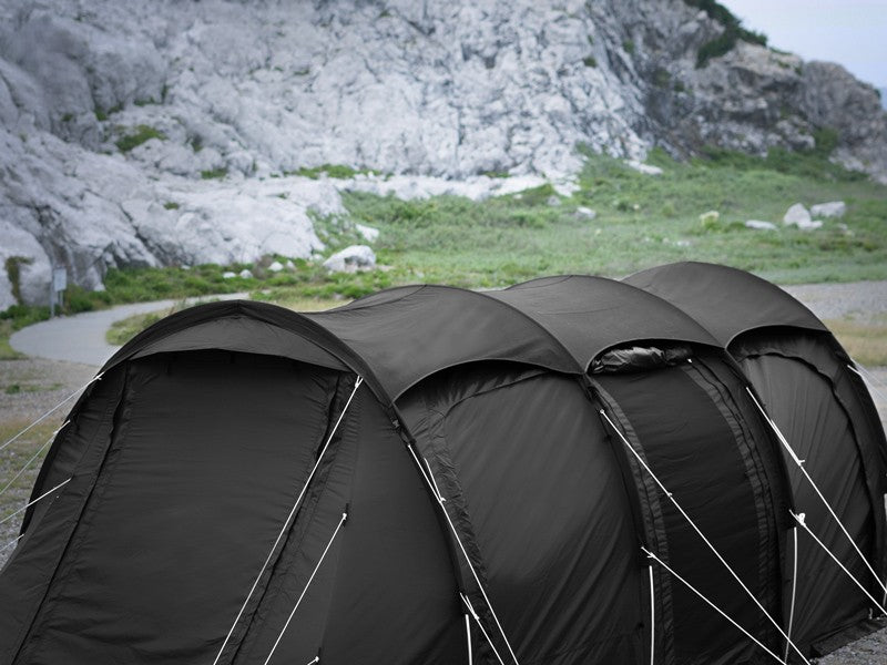 A large black multi-person camping tent pitched outdoors in a rocky, grassy mountain setting.